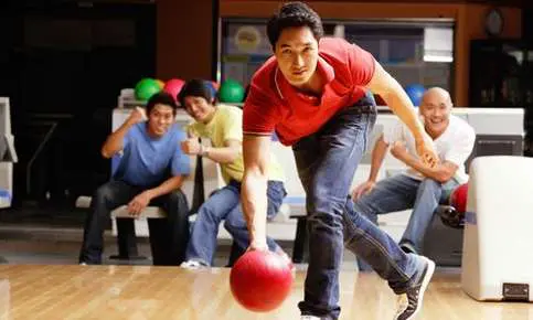 Person rolling bowling ball, friends watching
