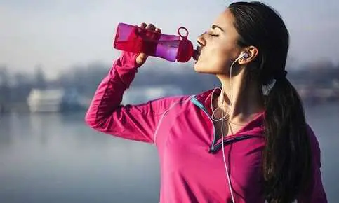 Female athlete rehydrating by a lake