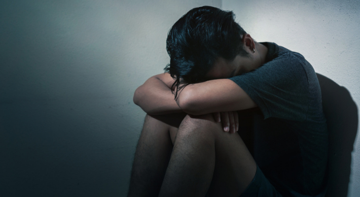 Man in shadow, hugging knees tightly