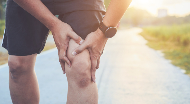 Person holding knee in pain outdoors