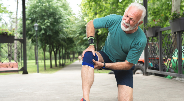 Elderly man holding painful knee outdoors
