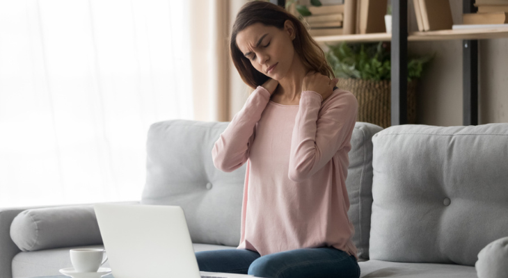 Woman massaging neck while sitting on couch