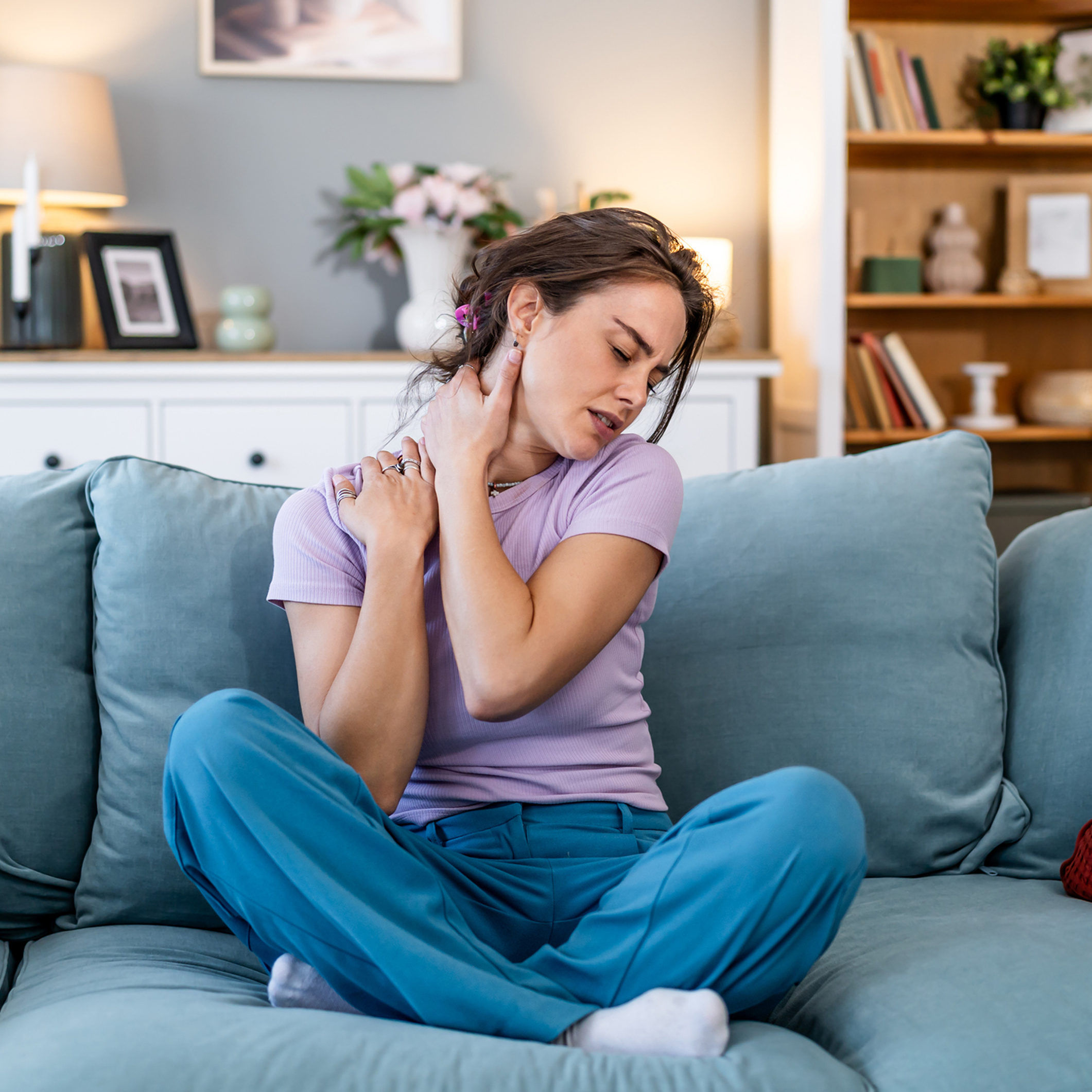 Woman massaging neck on blue sofa