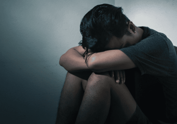Man in shadow, hugging knees tightly