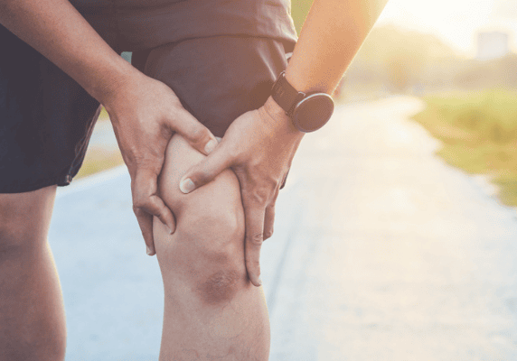Person holding knee in pain outdoors