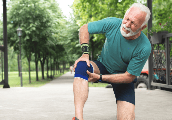 Elderly man holding painful knee outdoors